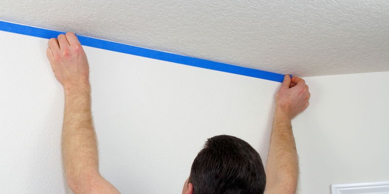 man applying blue painter's tape to wall
