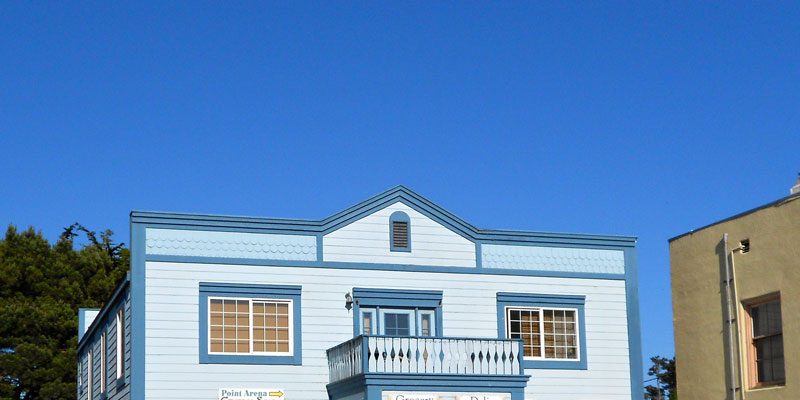 small-town shop with balcony painted light blue with darker blue accent with clear blue skies