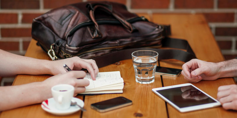 close-up of meeting between two people with one person taking notes on paper and other on tablet