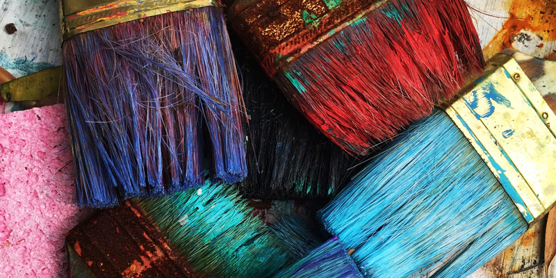 pile of used, colorful paint brushes and sponge on table