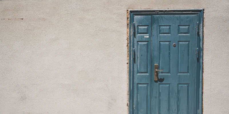 weathered side of stucco home with wooden door and fading paint