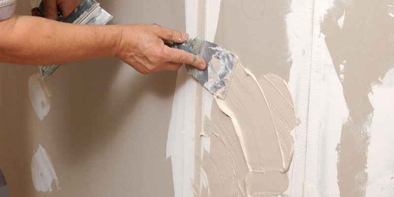 man patching hole in drywall with spackling paste and putty knife