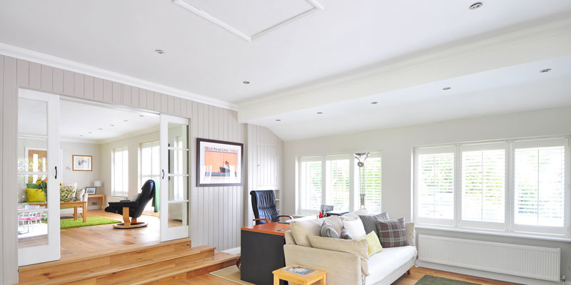 conjoined living rooms with white ceiling filled with couch, desk, and windows shining daylight