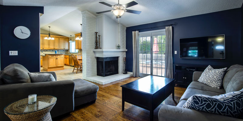 navy-painted living room with sofas and coffee table on wooden floor with fireplace in corner and ceiling fan