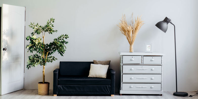 side of living room with love seat, plants, lamp, and chalky-painted dresser