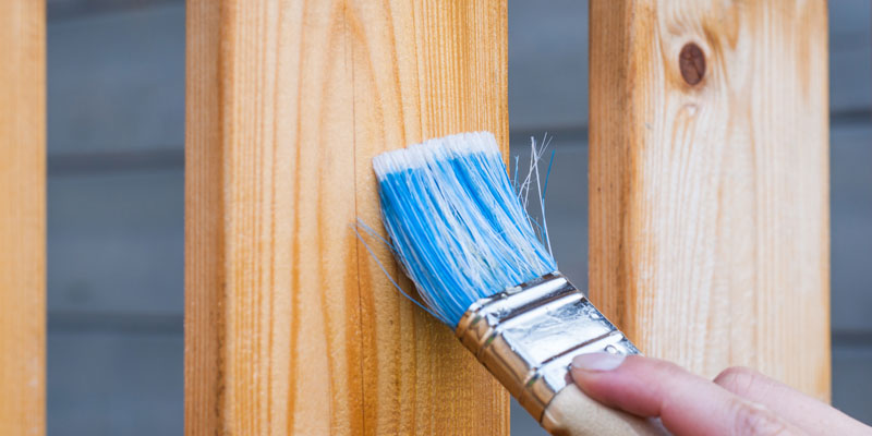 blue-bristled brush applying stain to wooden balcony boards