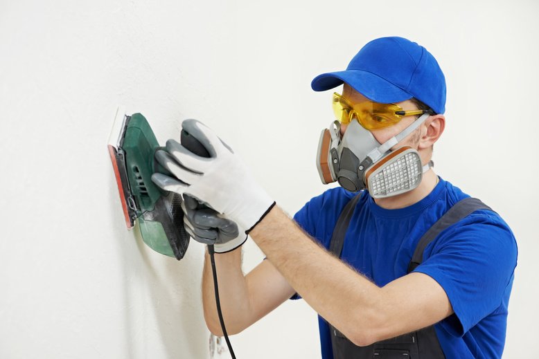 painter wearing a respirator while sanding wall to prepare for painting project