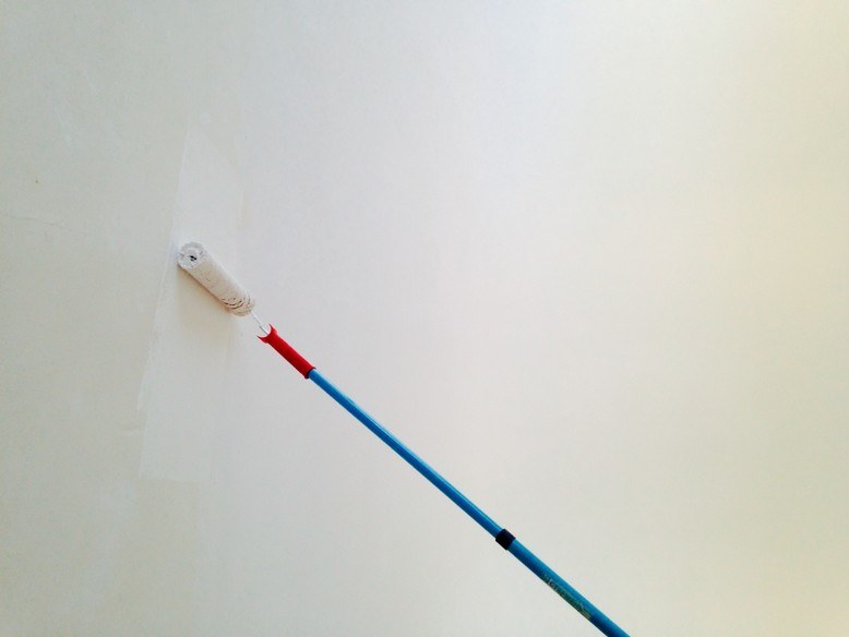 painter using paint roller to prime wall